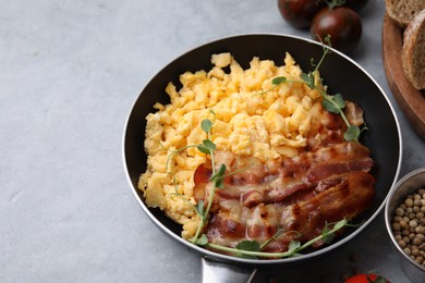 Delicious scrambled eggs with bacon in frying pan on grey table. Space for text