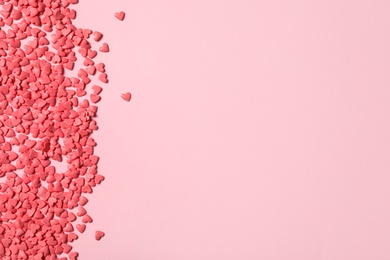 Photo of Heart shaped sprinkles on pink background, flat lay. Space for text