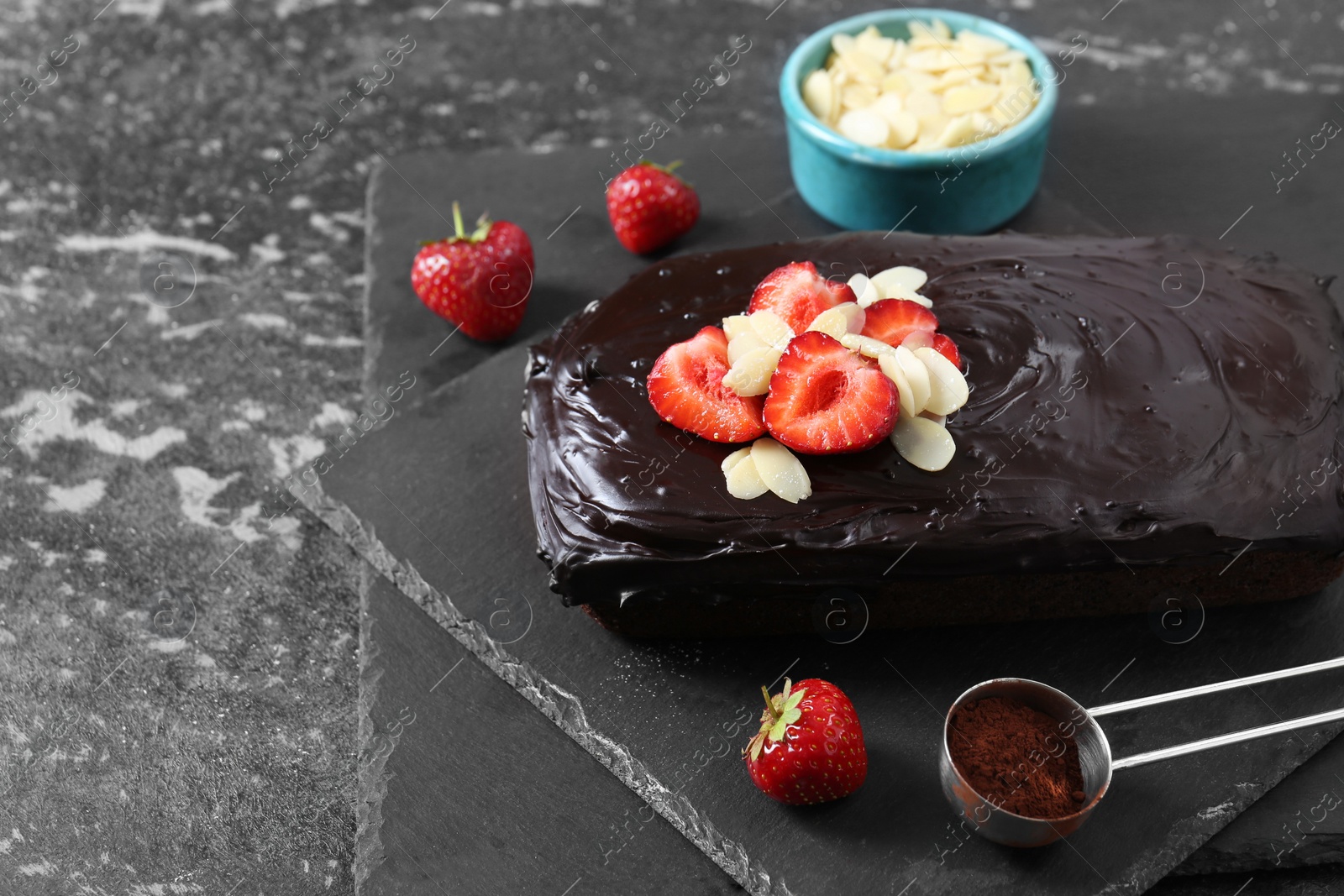 Photo of Delicious chocolate sponge cake with strawberry and almond flakes on black table