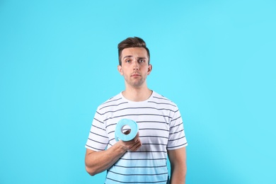 Young man holding toilet paper roll on color background