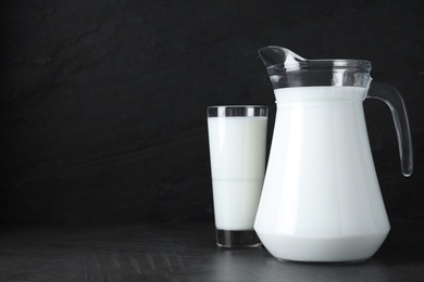 Photo of Jug and glass with fresh milk on black table. Space for text