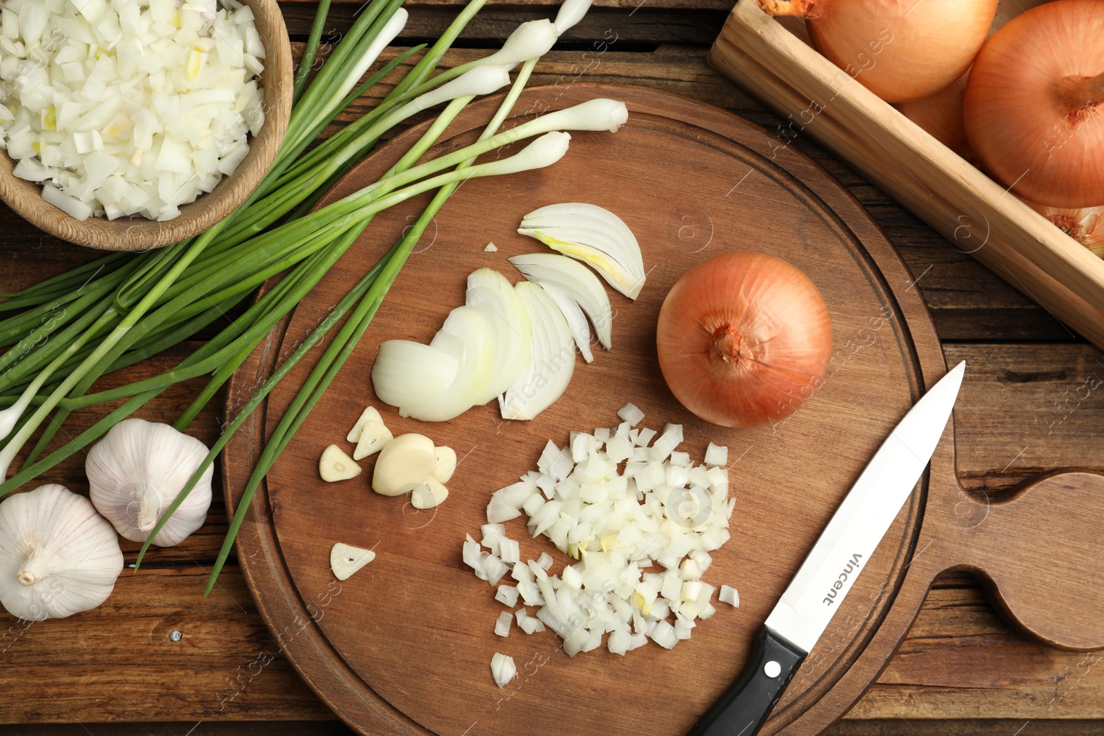 Photo of Board with cut onion and garlic on wooden table, flat lay