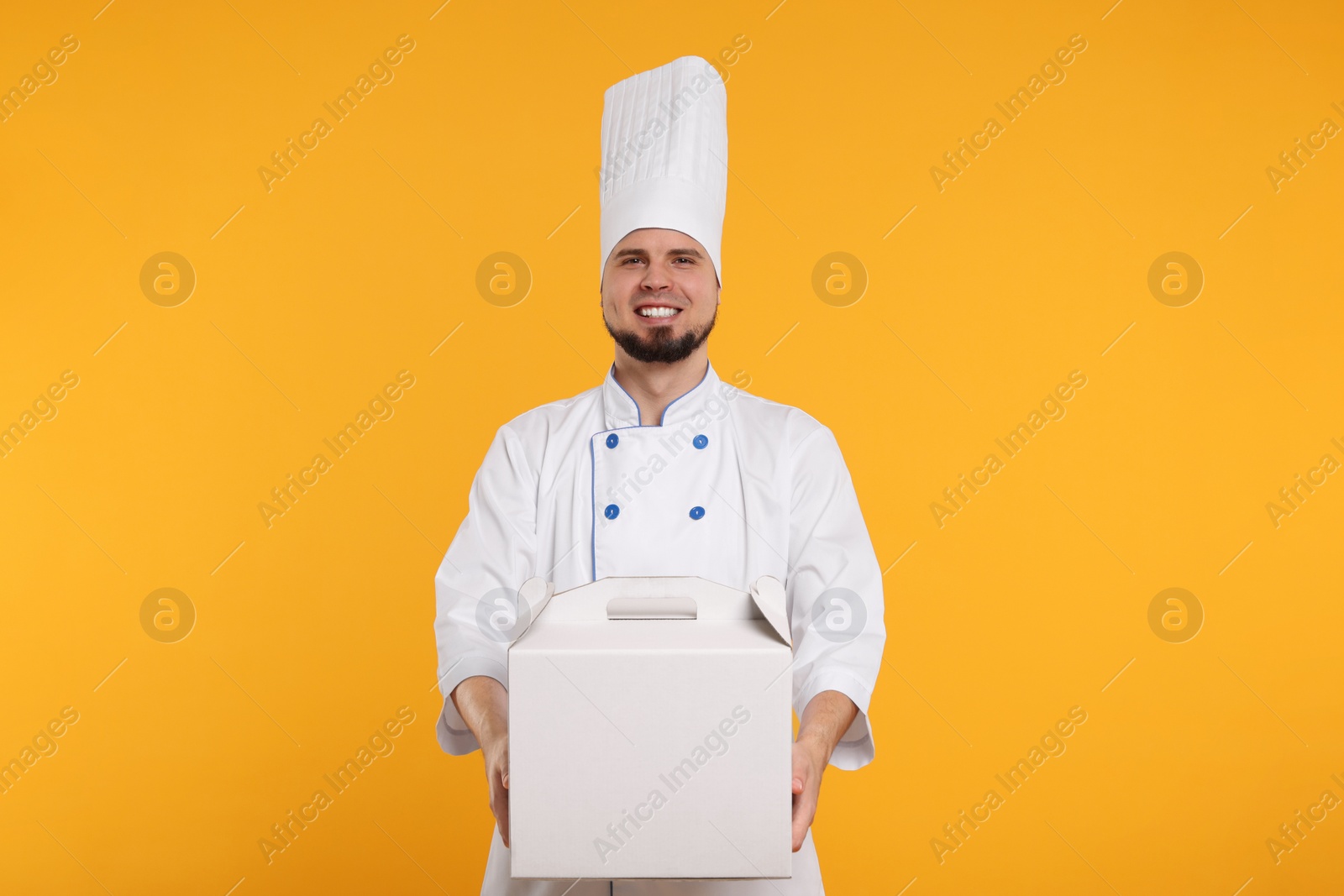 Photo of Happy professional confectioner in uniform holding cake box on yellow background