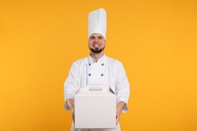 Happy professional confectioner in uniform holding cake box on yellow background