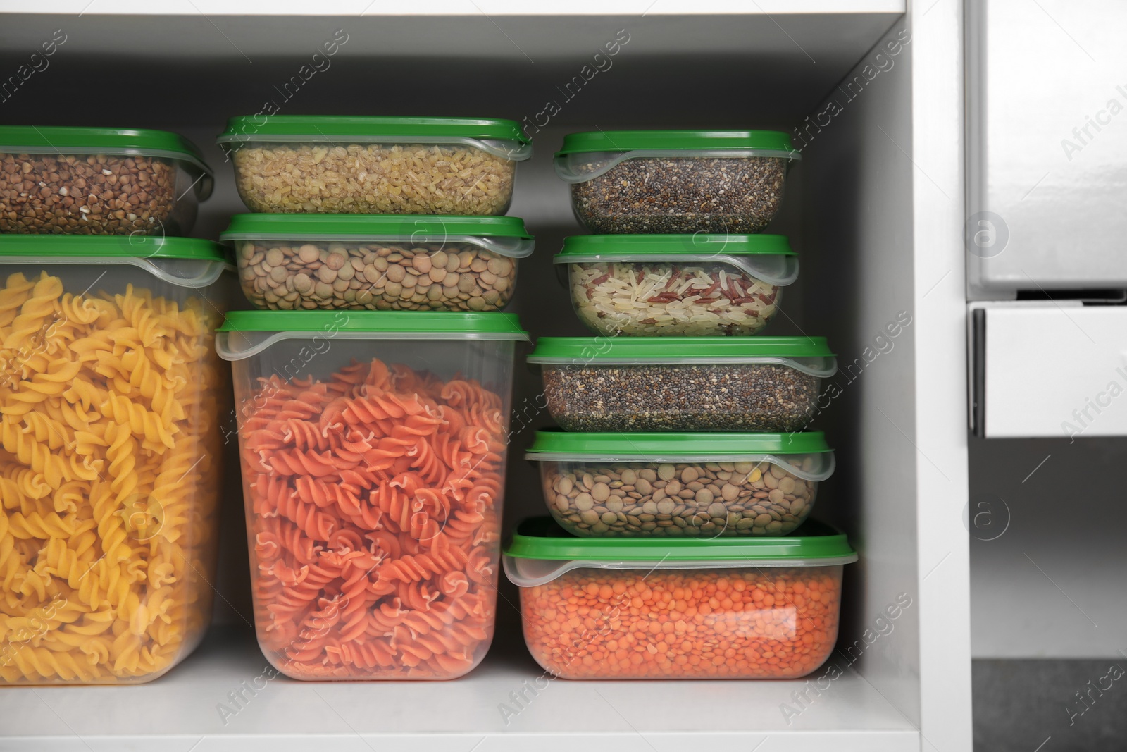 Photo of Plastic containers filled with food products in kitchen cabinet, closeup