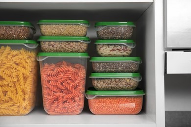 Plastic containers filled with food products in kitchen cabinet, closeup