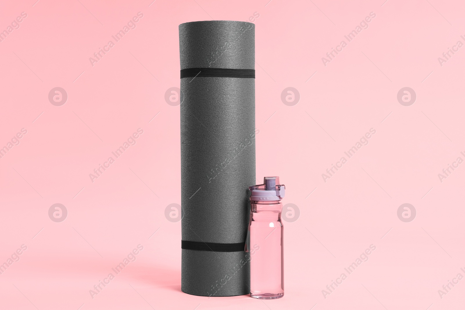 Photo of Grey yoga mat and bottle of water on pink background