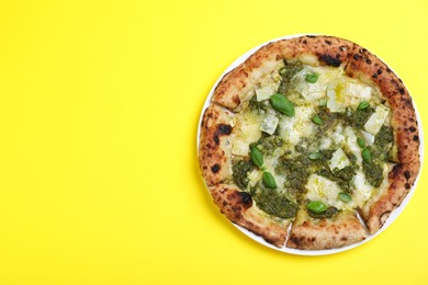 Photo of Delicious pizza with pesto, cheese and basil on yellow background, top view. Space for text