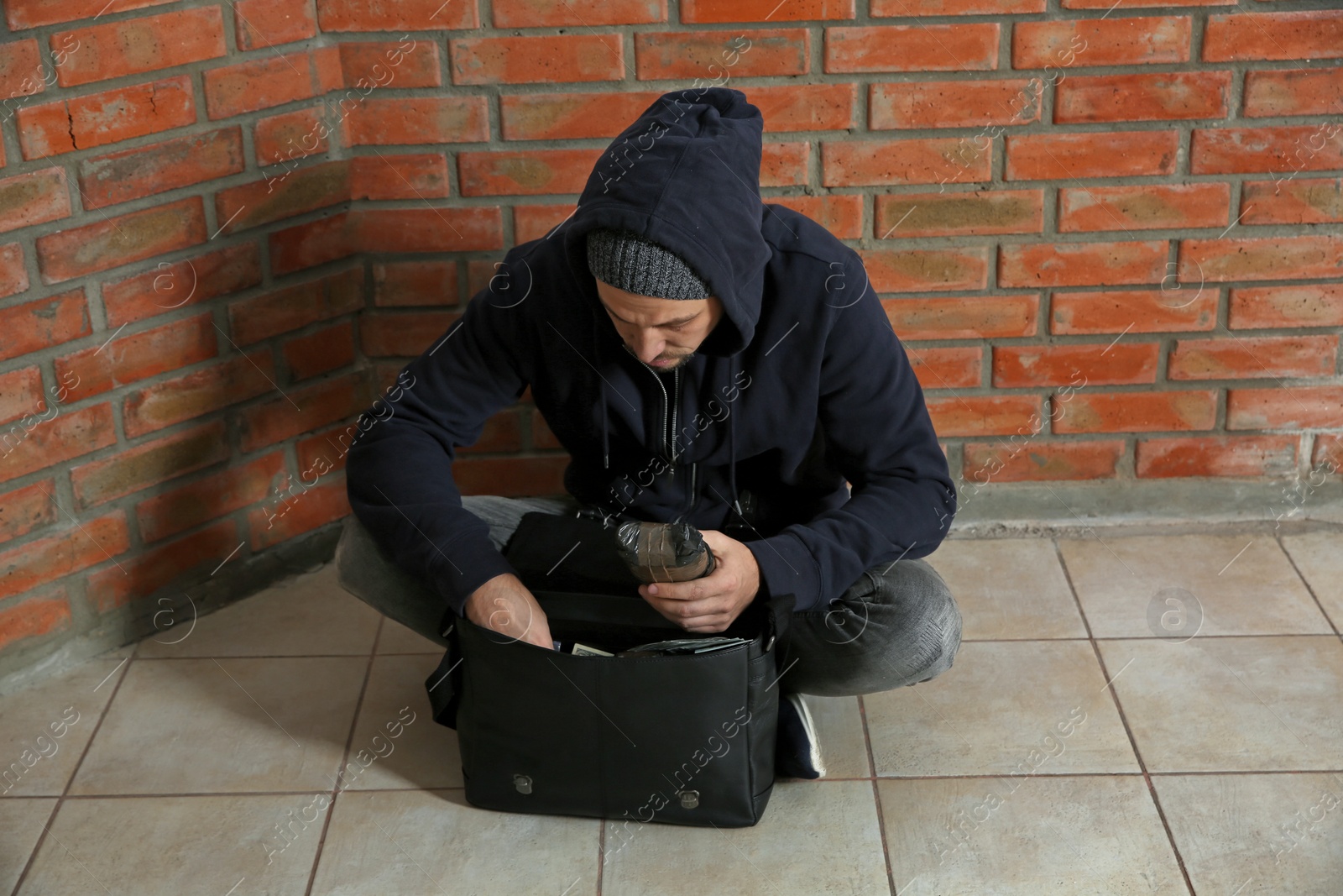 Photo of Drug dealer with narcotics sitting on floor against brick wall