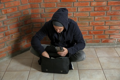 Photo of Drug dealer with narcotics sitting on floor against brick wall