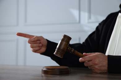Photo of Judge with gavel pointing and sitting at wooden table indoors, closeup