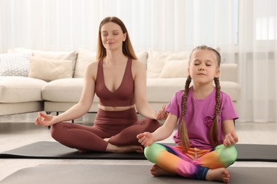 Photo of Mother with daughter in sportswear meditating together at home. Harmony and zen