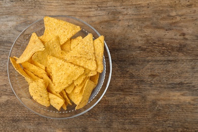 Photo of Glass bowl with tasty Mexican nachos chips on wooden table, top view. Space for text