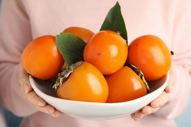 Photo of Woman holding bowl with delicious fresh persimmons, closeup