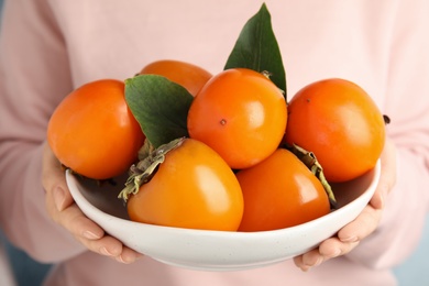 Woman holding bowl with delicious fresh persimmons, closeup