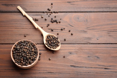 Photo of Bowl and spoon of black pepper corns on wooden table, flat lay with space for text