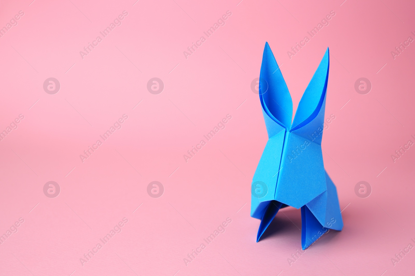 Photo of Origami art. Paper rabbit on pink background, space for text