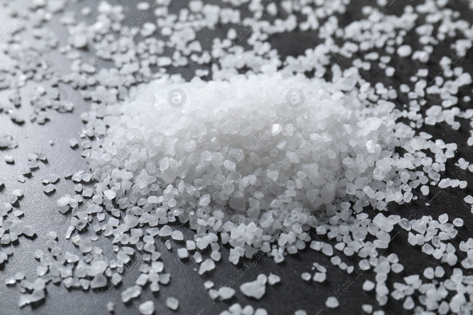 Photo of Heap of natural salt on black table, closeup