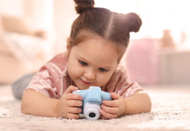 Photo of Little photographer with toy camera on floor at home