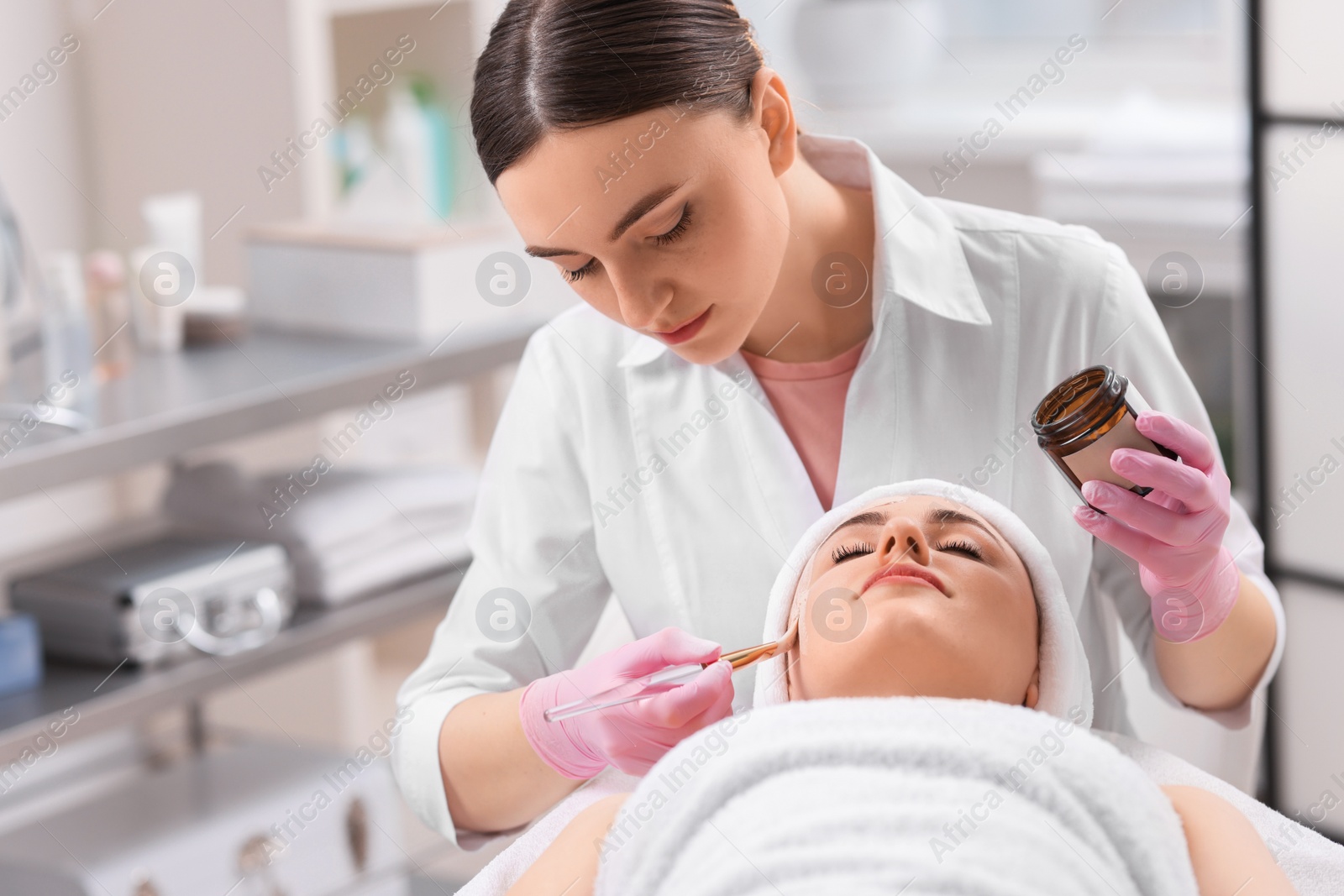 Photo of Cosmetologist applying mask on woman's face in clinic