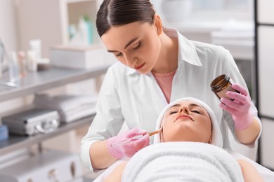 Photo of Cosmetologist applying mask on woman's face in clinic