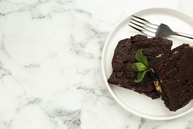 Photo of Delicious brownies with nuts and mint on white marble table, top view. Space for text