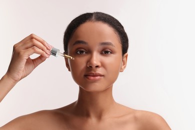 Beautiful woman applying serum onto her face on white background
