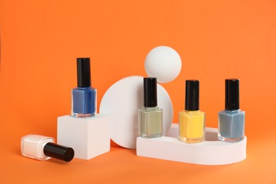 Photo of Stylish presentation of bright nail polishes in bottles on orange background