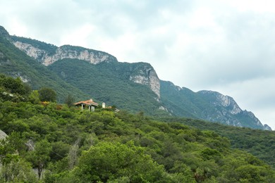 Photo of Picturesque view of estate near big mountains and trees under cloudy sky