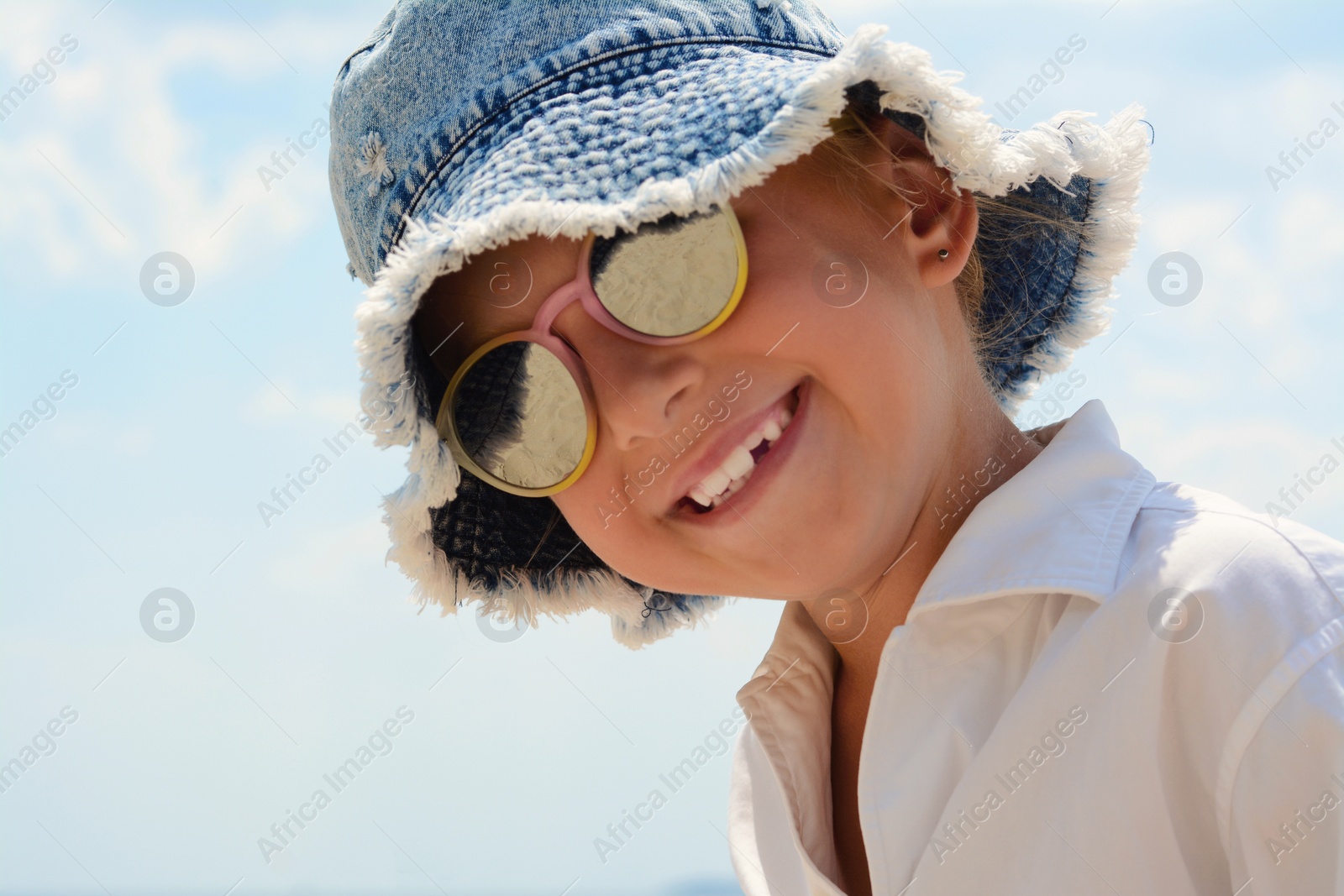 Photo of Little girl wearing sunglasses and hat at beach on sunny day