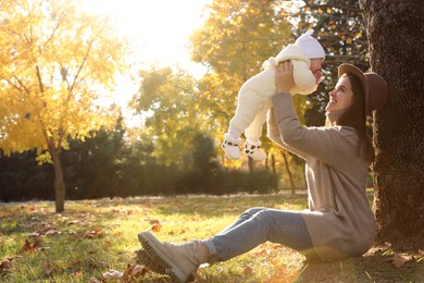 Happy mother with her baby daughter sitting near tree in park on sunny autumn day, space for text