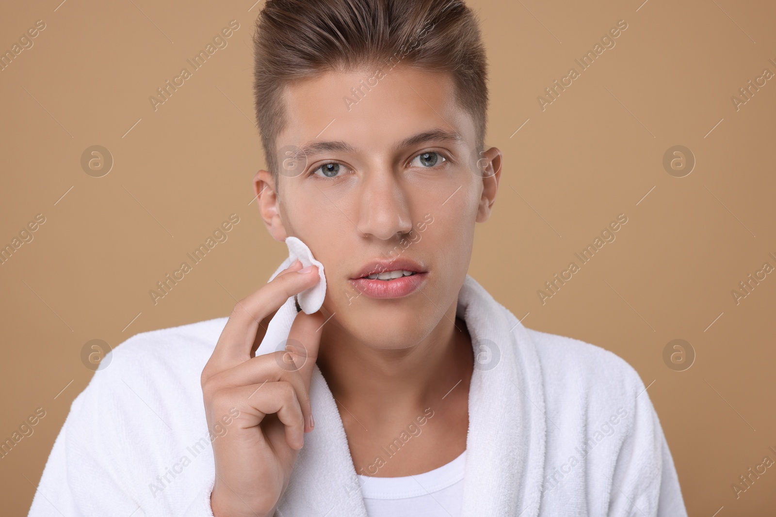 Photo of Handsome man cleaning face with cotton pad on beige background