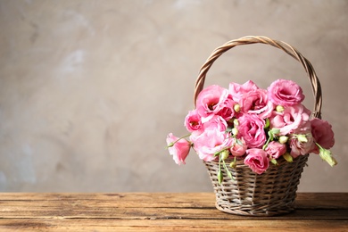 Photo of Beautiful pink Eustoma flowers in wicker basket on wooden table against grey background. Space for text
