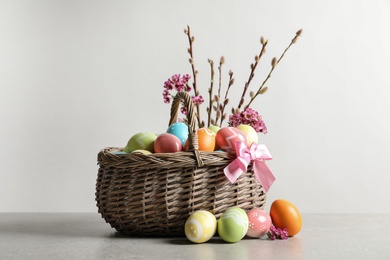 Wicker basket with painted Easter eggs and flowers on table