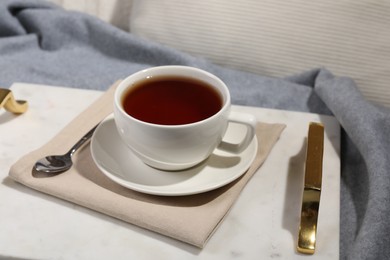 Photo of Aromatic tea in cup, saucer and spoon on table