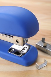 Blue stapler with staples on wooden table, closeup