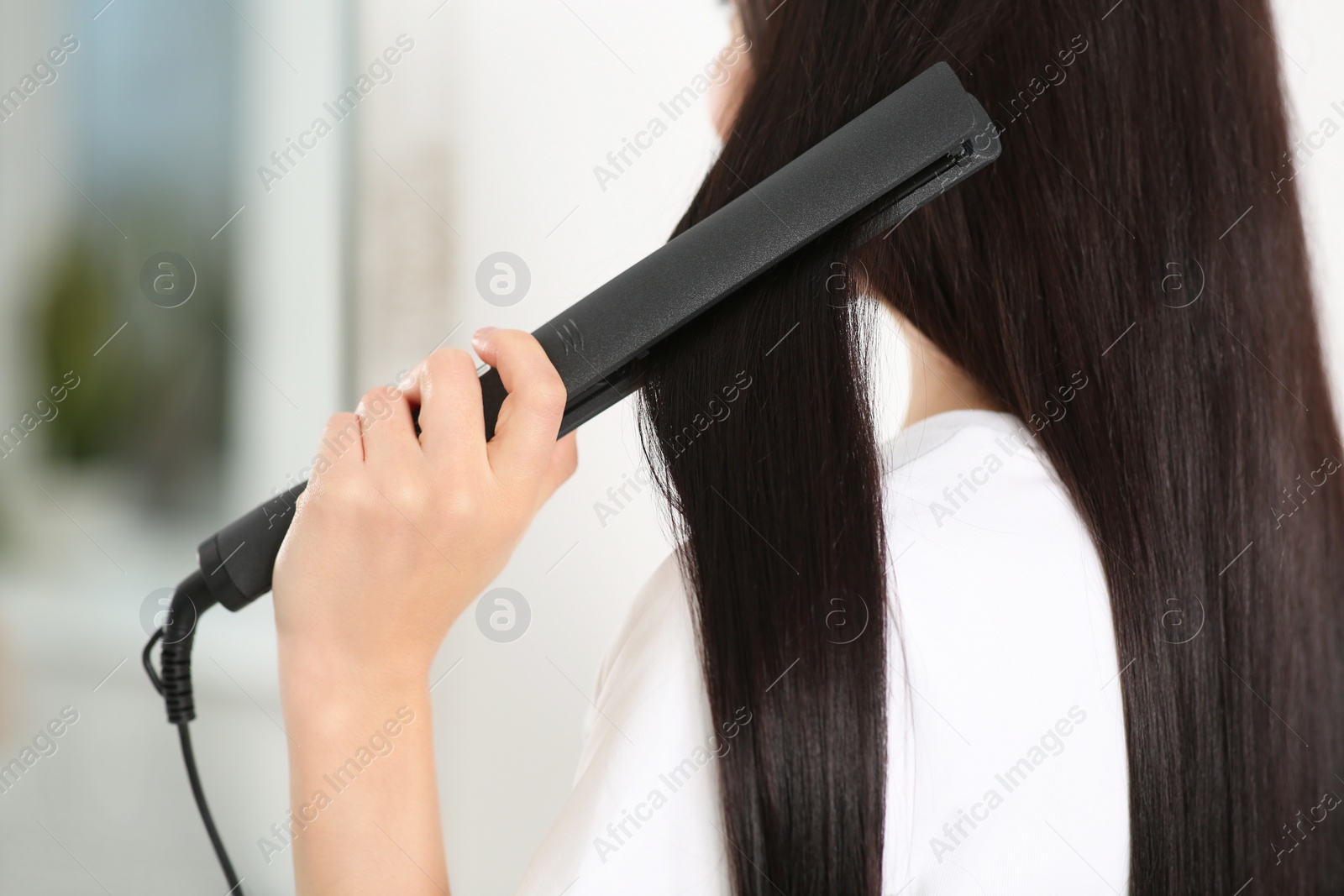 Photo of Woman using hair iron indoors, closeup view