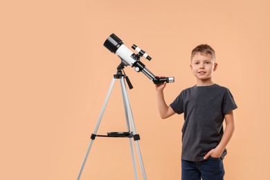 Cute little boy with telescope on beige background, space for text