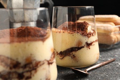 Photo of Delicious tiramisu in glasses and spoon on grey textured table, closeup