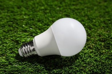 Photo of New light bulb on fresh green grass, closeup