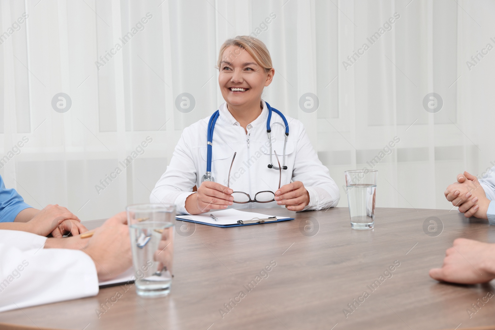 Photo of Medical conference. Professional doctor sitting at wooden table in clinic