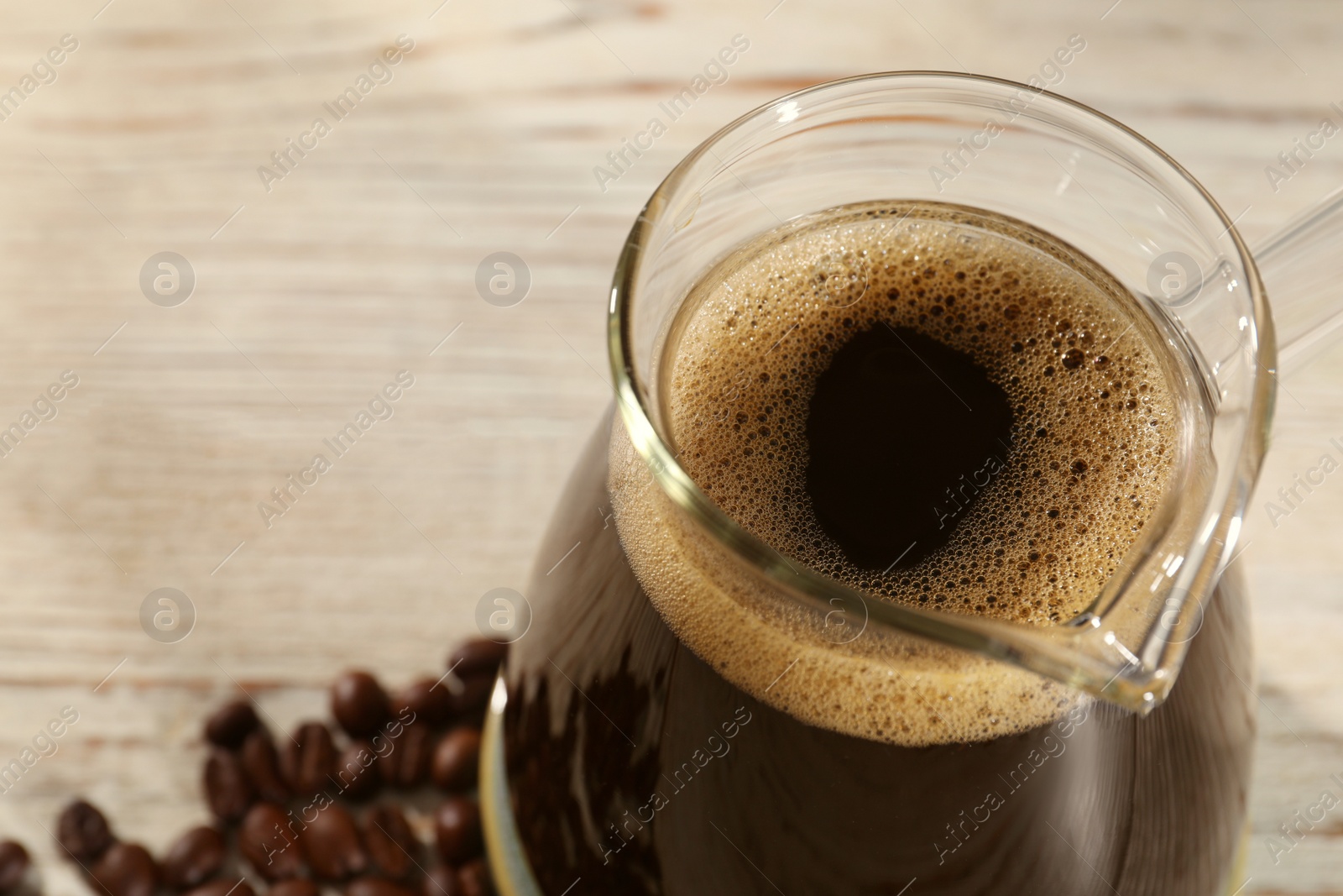 Photo of Glass turkish coffee pot with hot drink on wooden table, closeup. Space for text