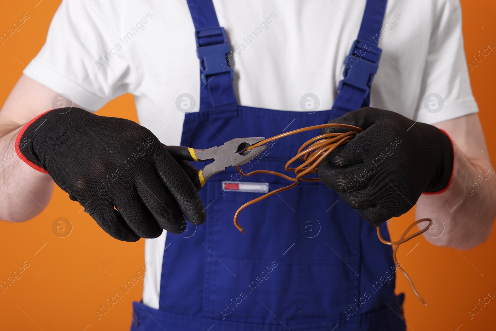 Photo of Young man holding pliers and wires on orange background, closeup