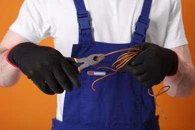 Photo of Young man holding pliers and wires on orange background, closeup