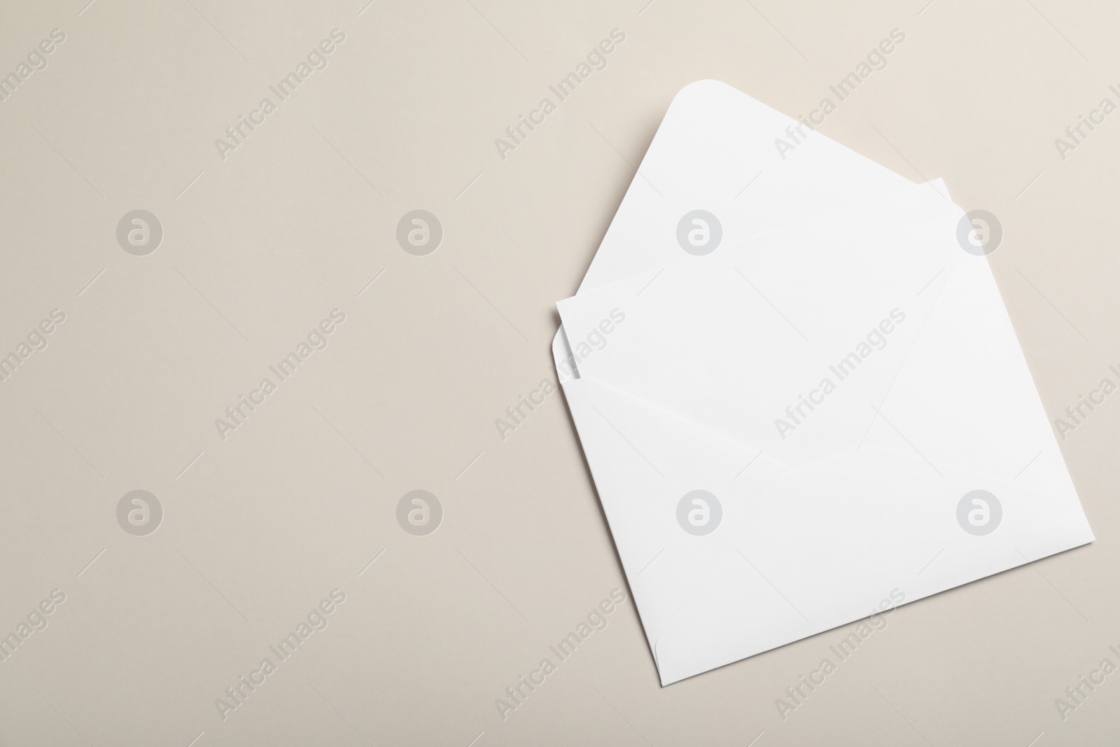 Photo of White paper envelope with blank card on beige background, top view. Space for text