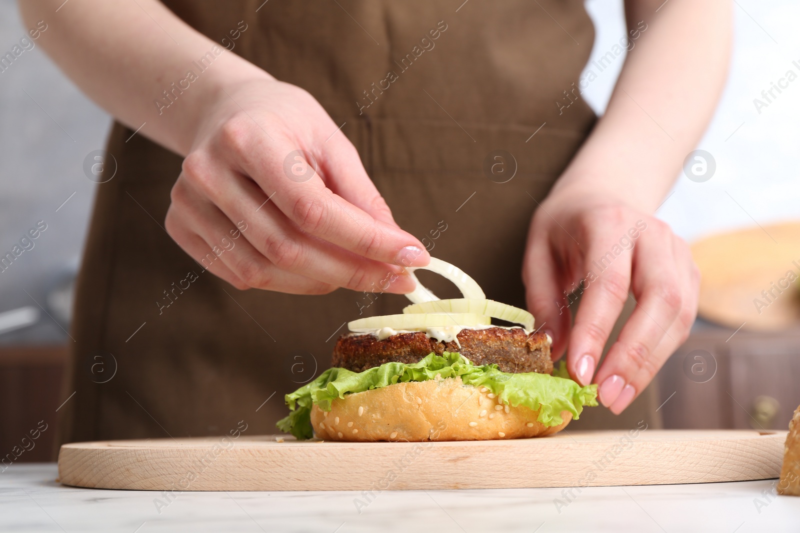 Photo of Woman making delicious vegetarian burger at table, closeup