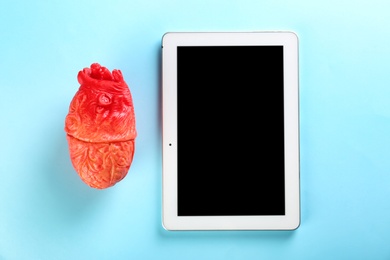 Photo of Tablet and model of heart on color background. Heart attack concept
