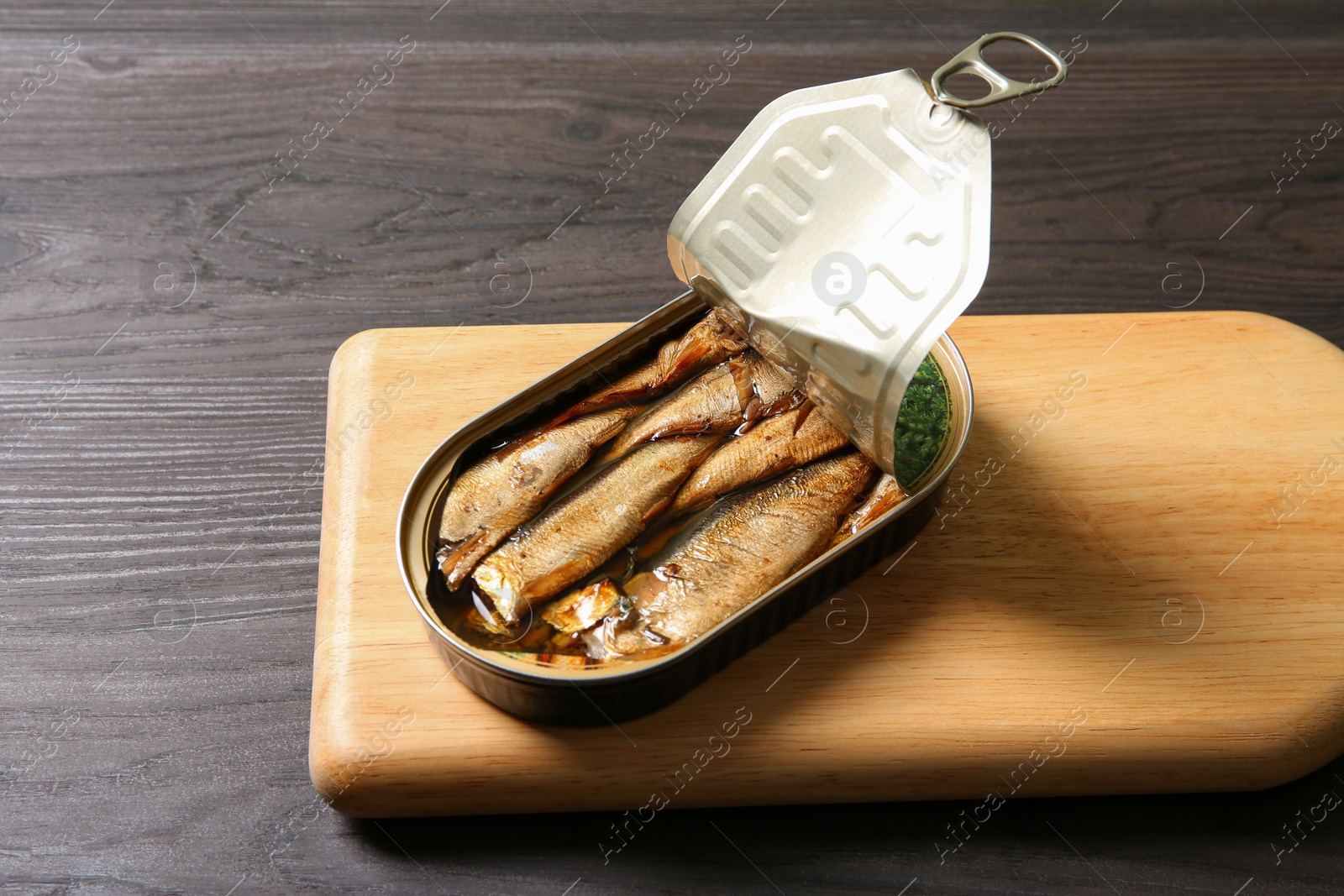Photo of Board with tin can of sprats on wooden table