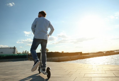 Photo of Man riding kick scooter along city street on sunny day
