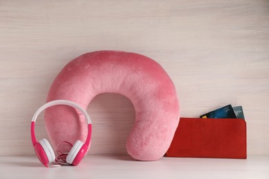 Photo of Pink travel pillow, wallet with credit cards and headphones on light wooden background